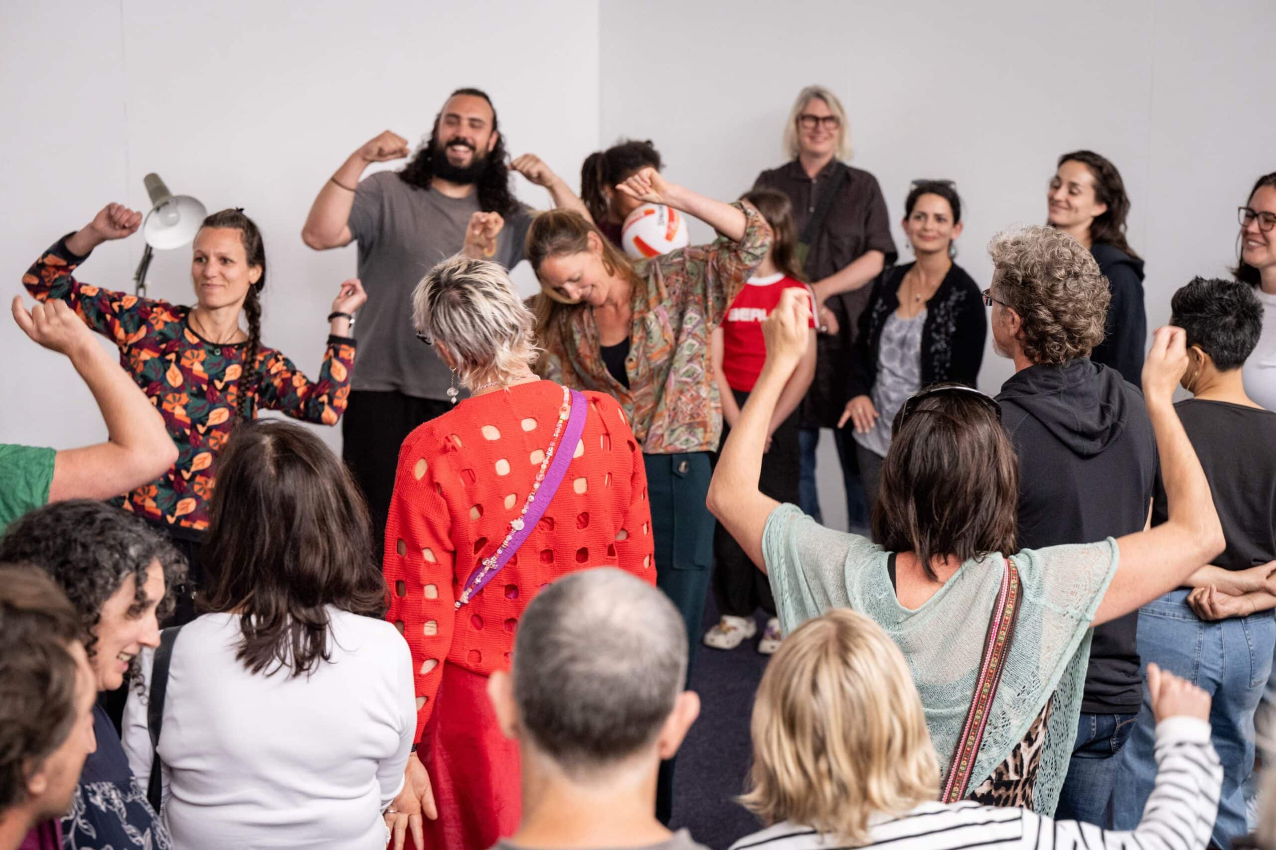 lots of people standing and sitting around a room, engaging with their hands in the air